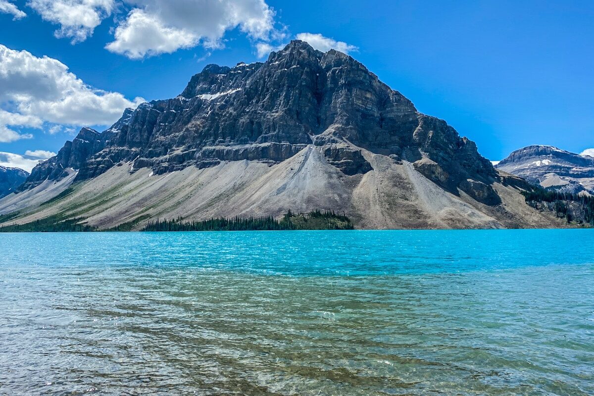 A dramatic grey coloured mountain with a jagged peak towers of a bright vibrant blue lake.