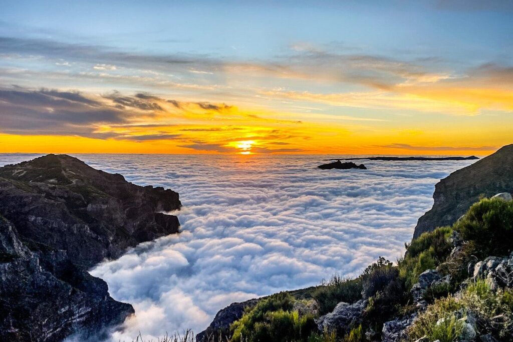 A blanket of cloud covers the sky as the mountain peaks of Madeira peep above the cloud inversion. The sun is about to set below the clouds with a magnificent view and glow.