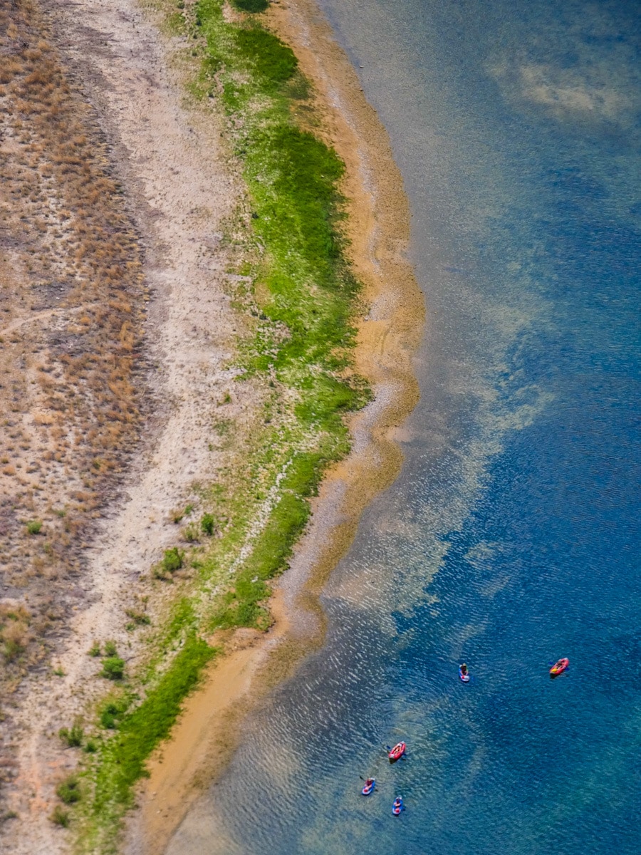 A bird's eye view of the Colorado River and shoreline. Three canoes can be seen from a distance.