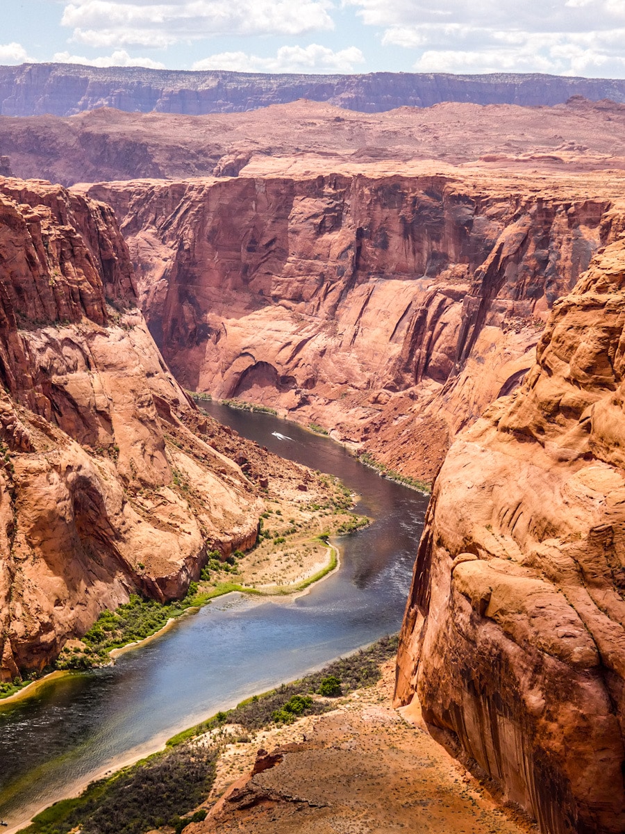 A boat is seen on the Colorado River in Horseshoe Bend. The red rock canyon walls tower above the river.