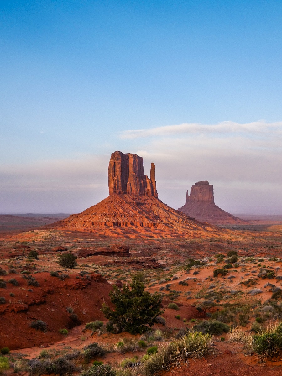 Red rocks from the buttes of Monument Valley sit in the sunrise of the desert.