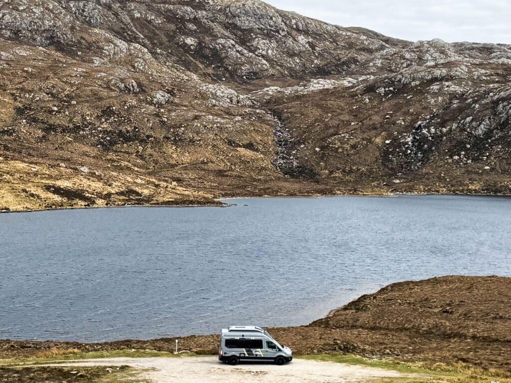View of a campervan overlooking a remote loch in Scotland as part of the route on the NC500 on a Scotland road trip in the UK.