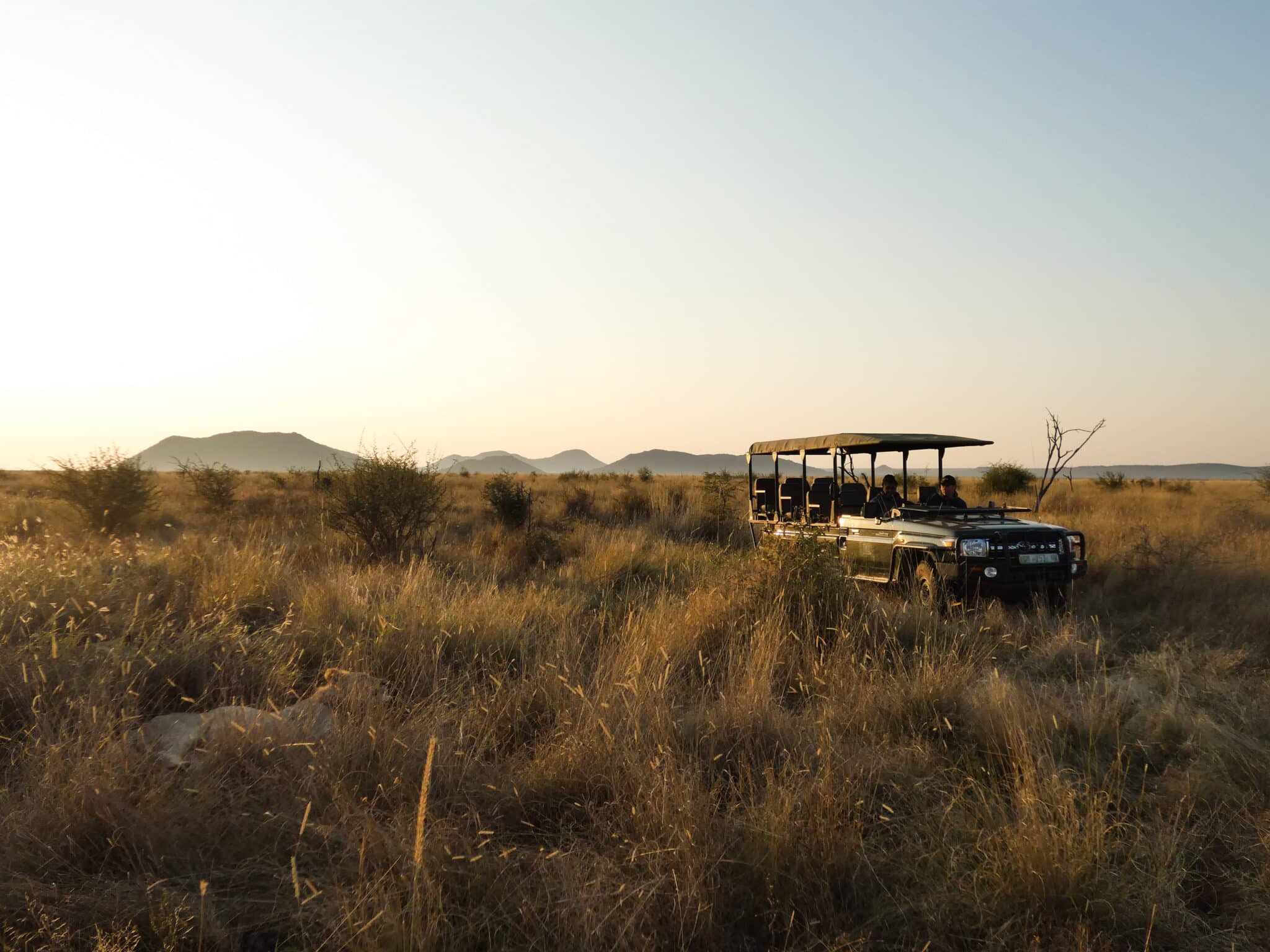 A safari jeep sits in the African bush as the sun rises behind it.