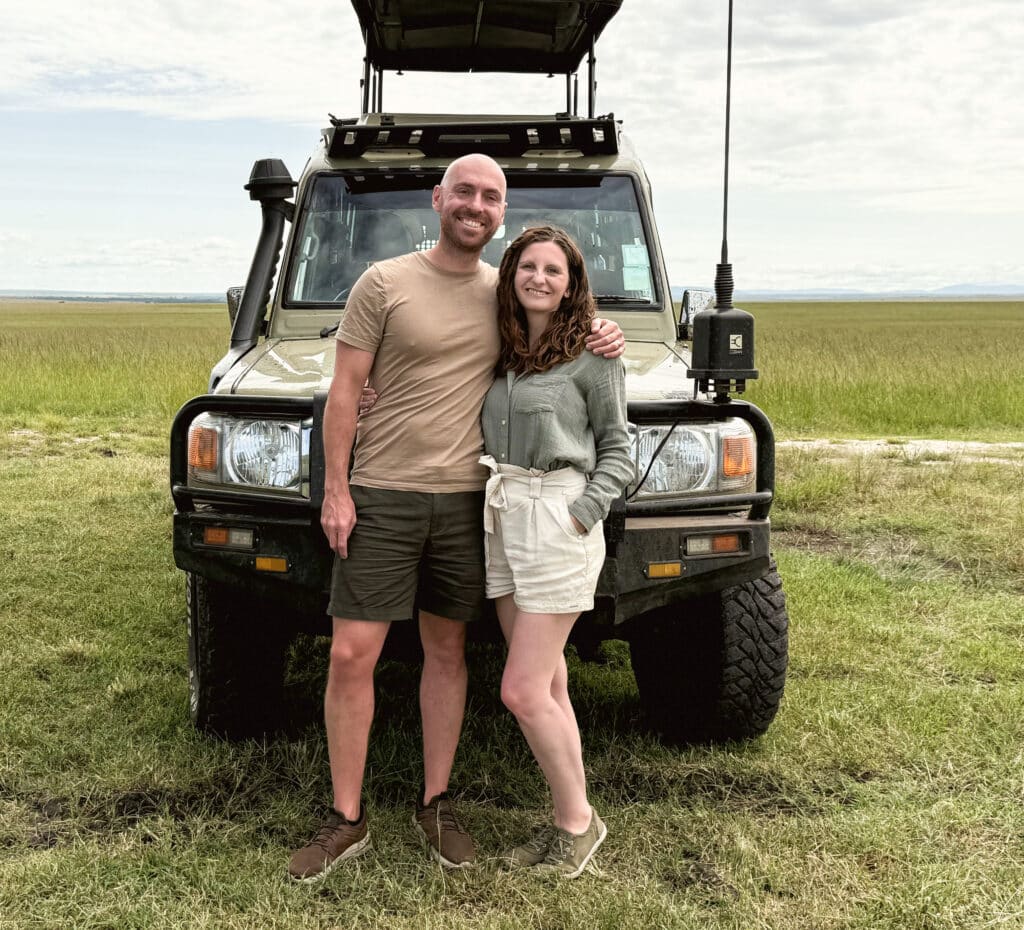 Mr and Mrs D Adventures on safari, standing in front of a safari jeep in the Maasai Mara. Book your safari through us.